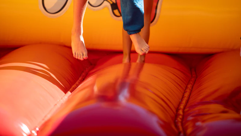 Children bouncing barefoot on a bright orange bouncy castle in golden light