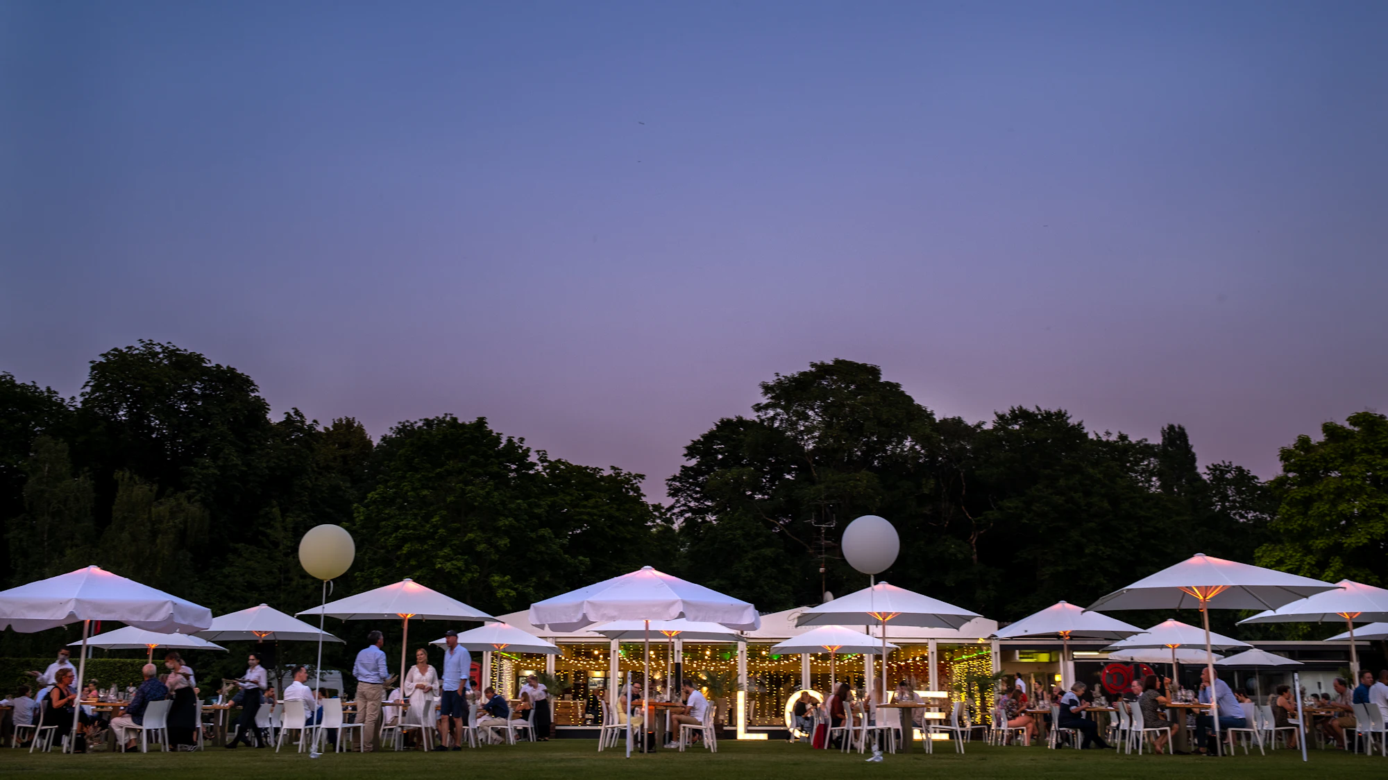 Company summer party under parasols and glowing lights at dusk