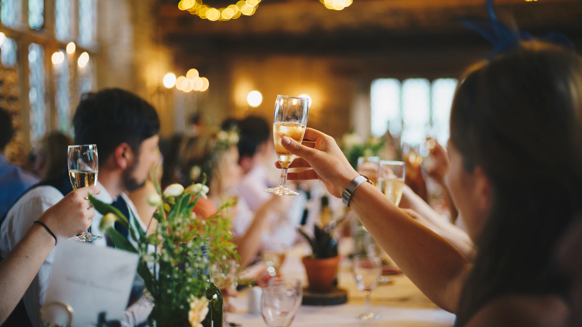 Guests raising champagne glasses beneath festoon lights at a milestone celebration